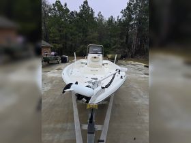A clear view of a center console boat docked on a concrete surface, surrounded by trees, showcasing its sleek design and features.