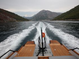 A stunning view of a boat in motion, cutting through calm waters with mountainous scenery in the background — perfect for showcasing the beauty of coastal adventures.