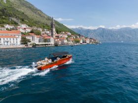 A vibrant boat glides through the clear waters, showcasing stunning coastal scenery and mountains in the background — a perfect snapshot of a memorable boating adventure.