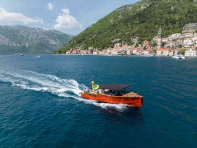 A vibrant boat glides through clear waters, showcasing stunning coastal scenery and charming hillside villages — perfect for exploring the beautiful coastline.