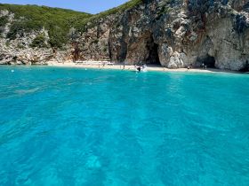 A stunning view of a secluded beach with crystal-clear waters, where visitors enjoy the sun and swimming — a perfect destination for a day of relaxation and adventure.