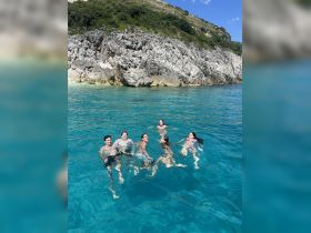 A lively group enjoys a refreshing swim in crystal-clear waters, surrounded by stunning rocky cliffs — perfect for a fun day out on the water.