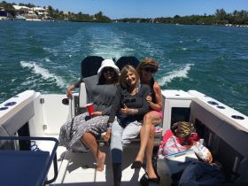 A joyful group of friends enjoys a sunny day on the water, relaxing on a boat with drinks in hand — perfect for a fun day out on the waves.