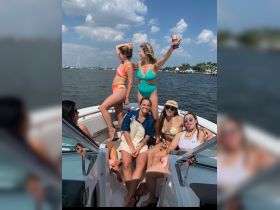 A lively group of friends enjoys a fun day on the water, showcasing their vibrant swimsuits and drinks aboard a boat — perfect for summer celebrations and memorable outings.