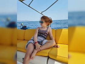 A young girl relaxes on a bright yellow seat aboard a boat, enjoying the serene ocean view — a perfect moment for family outings on the water.