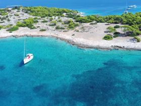 A stunning aerial view of a sailboat anchored in crystal-clear turquoise waters, surrounded by lush greenery and rocky shores — an ideal setting for serene sailing adventures.