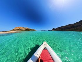 A stunning aerial view from the bow of a boat cruising through crystal-clear turquoise waters, showcasing the beautiful coastline and rocky formations in the distance.