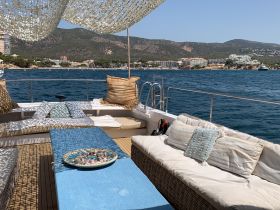 A cozy lounge area on a boat featuring comfortable seating and a decorative table, perfect for relaxing while enjoying the scenic views of the coastline.