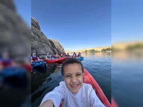 A joyful child takes a selfie while kayaking with a group, showcasing the fun of outdoor adventures on the water.