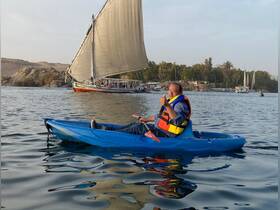 A kayaker gives a thumbs up while paddling on calm waters, with traditional sailboats in the background — a perfect snapshot of adventure and leisure on the water.