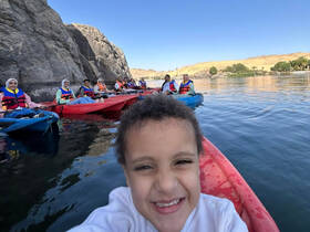A joyful group of kayakers, including a smiling child, enjoying a scenic adventure on the water, surrounded by stunning rock formations.