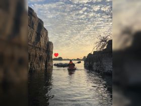 A kayaker paddles through a serene waterway at sunset, framed by rocky cliffs — a perfect moment for adventure seekers and nature lovers.