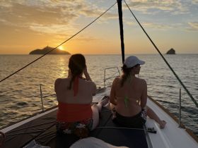 Two women enjoy a serene sunset view from the deck of a yacht, capturing the perfect moment against a picturesque island backdrop.