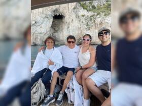 A joyful group of family members poses together on a boat, enjoying their time near a stunning coastal cave — perfect for memorable outings and family adventures.
