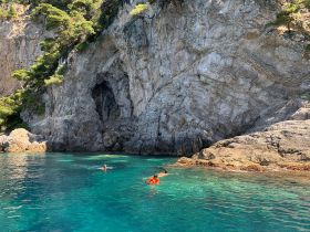 Two swimmers enjoy the crystal-clear waters near a stunning rocky coastline, perfect for snorkeling and exploring marine life.