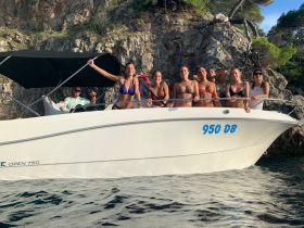 A lively group of friends enjoys their time aboard a boat, celebrating against a stunning rocky backdrop — perfect for summer adventures and memorable outings.