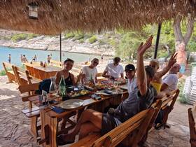 A lively group enjoys a meal together at a beachside restaurant, celebrating with food and drinks while surrounded by beautiful coastal scenery.