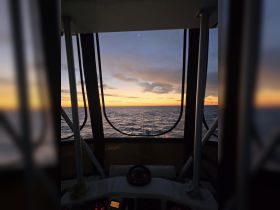 A serene view from the helm of a boat, showcasing a stunning sunset over the water — perfect for capturing the essence of a peaceful evening cruise.