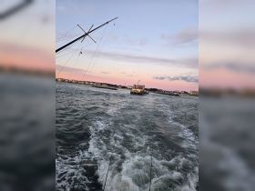 A scenic view of a fishing boat navigating through the water at sunset, showcasing the beauty of a tranquil evening on the sea.