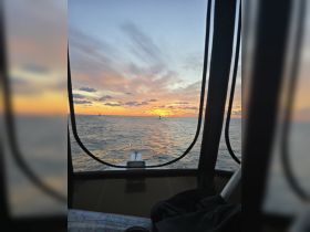A stunning sunset view from the bow of a boat, showcasing the tranquil waters and vibrant sky — perfect for evening cruises.