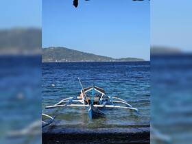 A traditional outrigger boat is docked in clear waters, set against a backdrop of lush hills and a serene blue sky, perfect for exploring coastal destinations.