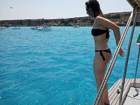 A woman prepares to jump into the crystal-clear waters from the side of a boat, capturing the essence of summer fun and adventure on the water.