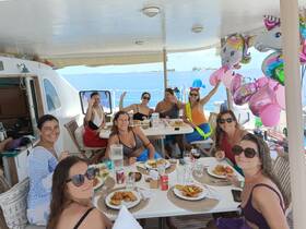 A lively group of friends enjoys a festive meal aboard a boat, complete with balloons and smiles, perfect for celebrations on the water.