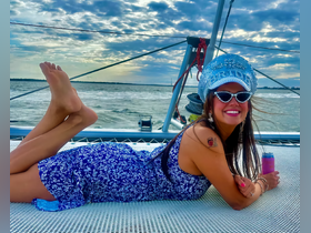 A joyful woman lounges on the deck of a yacht, enjoying the sunset with a drink in hand — perfect for celebrations and memorable moments on the water.