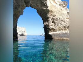 A stunning view through a natural rock arch towards a catamaran anchored in calm waters, showcasing the beauty of coastal landscapes.