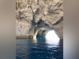 A stunning view of a cave entrance illuminated by sunlight, reflecting off the tranquil waters — a picturesque destination for boating adventures.