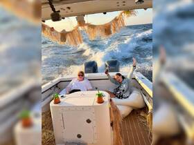 Two friends enjoy a lively moment aboard a boat, complete with tropical cocktails and a beautiful sunset backdrop — perfect for memorable boating adventures.