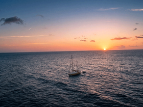A serene sunset view of a sailboat gracefully sailing across the ocean, creating a picturesque scene perfect for romantic getaways or peaceful sailing adventures.
