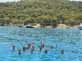 A lively group of friends enjoys a refreshing swim in crystal-clear waters, celebrating their day out on the boat amidst beautiful scenery.