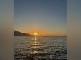 A stunning sunset over tranquil waters, with silhouetted mountains in the background — a perfect scene for evening boat cruises.