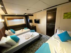 A cozy boat cabin featuring two beds with vibrant blue pillows and neatly arranged towels, perfect for comfortable overnight stays on the water.