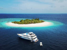 A stunning aerial view of a luxurious yacht anchored near a pristine sandbar, surrounded by vibrant turquoise waters and lush greenery — an ideal setting for tropical getaways.
