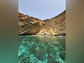 A stunning view of a rocky coastline with crystal-clear waters, featuring a person enjoying the serene environment — perfect for eco tours and beach explorations.