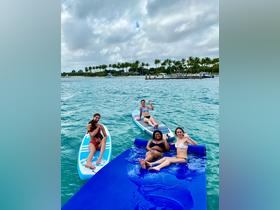 A lively group enjoys a fun day on the water, paddleboarding and relaxing on a floating mat — perfect for summer adventures and beach outings.