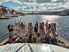 A lively group of women celebrates on the deck of a boat, enjoying drinks and dancing under the sun — perfect for a fun day out on the water.