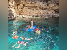 A lively group of children enjoys a fun day of swimming and paddleboarding in crystal-clear waters, surrounded by stunning rock formations — perfect for family adventures.