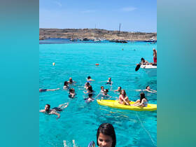 A lively scene of people enjoying the crystal-clear waters, swimming and kayaking, perfect for a fun day at the beach.