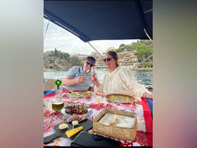 A couple enjoys a toast with cocktails while dining on a boat, surrounded by scenic views — perfect for romantic getaways or special celebrations on the water.