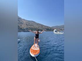 A woman joyfully paddleboards in clear blue waters, showcasing the fun and excitement of outdoor water activities under the sun.