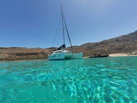 A stunning view of a catamaran anchored in crystal-clear turquoise waters, set against a backdrop of rugged hills — perfect for exploring coastal destinations.