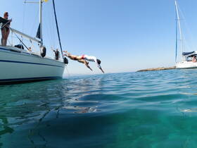 A thrilling moment captured as a group enjoys diving off a sailboat into crystal-clear waters, perfect for summer adventures and fun on the water.