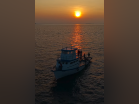 A group of people enjoy a sunset fishing trip aboard a boat, creating a picturesque scene on the open ocean.