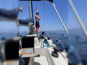 A man enjoys a moment on the deck of a sailboat, taking in the serene ocean views under a clear blue sky — a perfect day for sailing adventures.