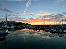A serene sunset view over a marina filled with various boats, reflecting the vibrant colors of the sky — a picturesque scene for boating enthusiasts.