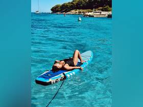 A woman relaxes on a paddleboard in crystal-clear waters, enjoying the sun and the serene surroundings — a perfect moment for water sports enthusiasts.