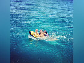 A joyful family enjoys a fun water activity, riding a yellow float in the clear blue ocean — perfect for summer adventures and family bonding.